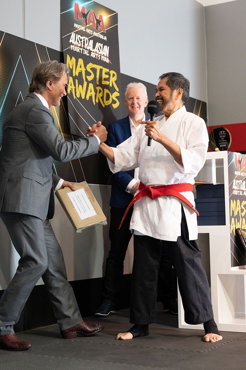 A man in a karate uniform is standing in front of a sign that says master awards.