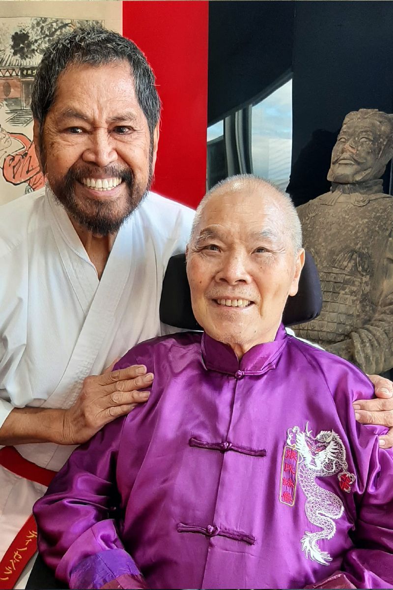 A man in a karate uniform is standing next to a man in a wheelchair.