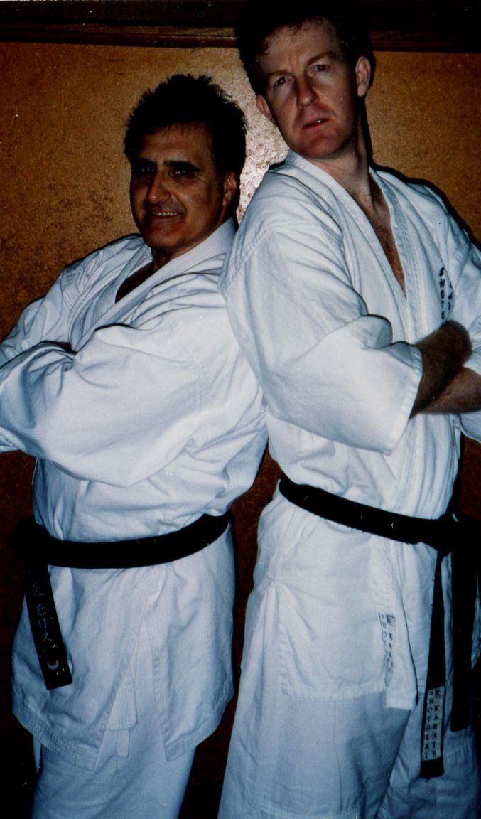 Two men in white karate uniforms are posing for a picture