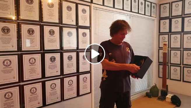 Man with many certificates on the wall, opening a box. Room with blinds, action taking place.
