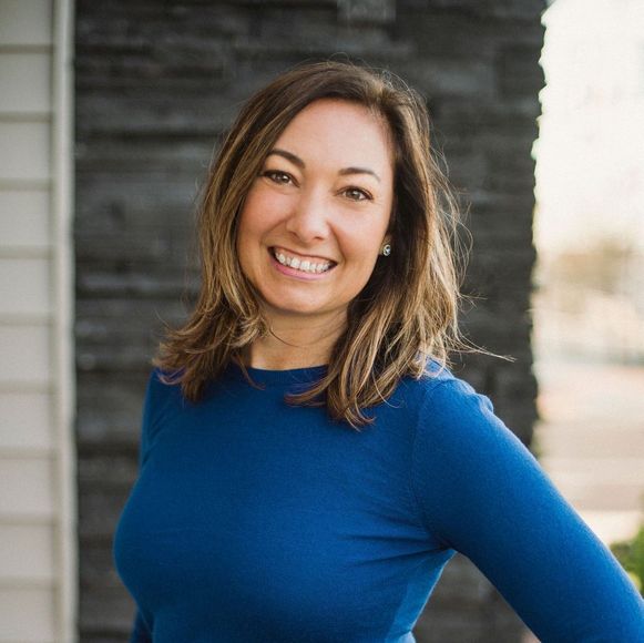 The woman is wearing a blue sweater and smiling for the camera.