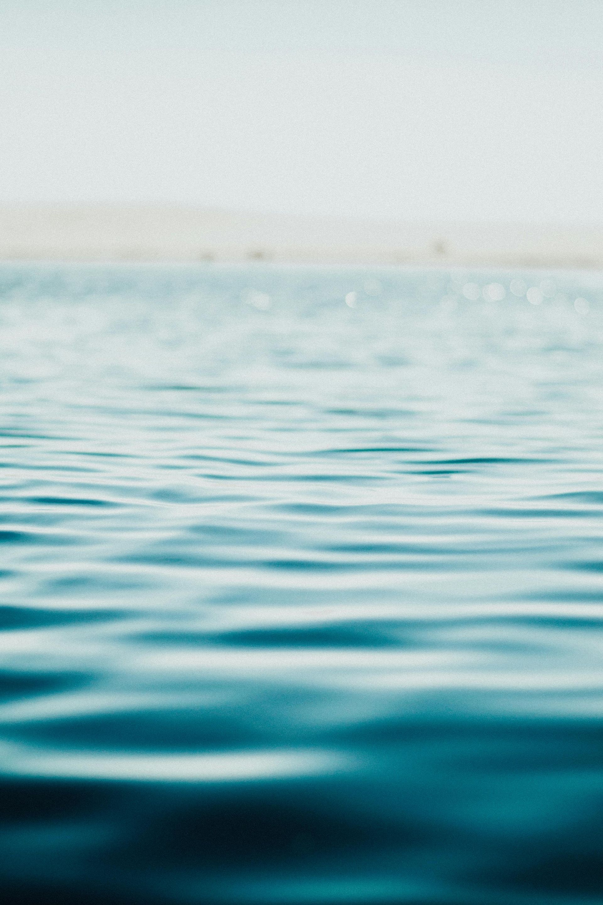 A close up of a body of water with waves and a white sky in the background.