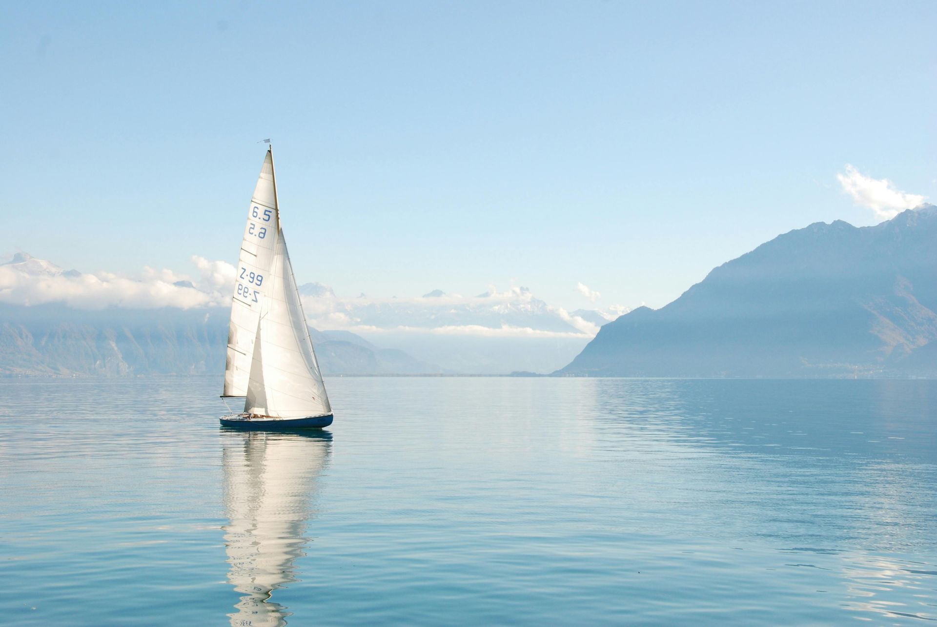 A sailboat is floating on a lake with mountains in the background.