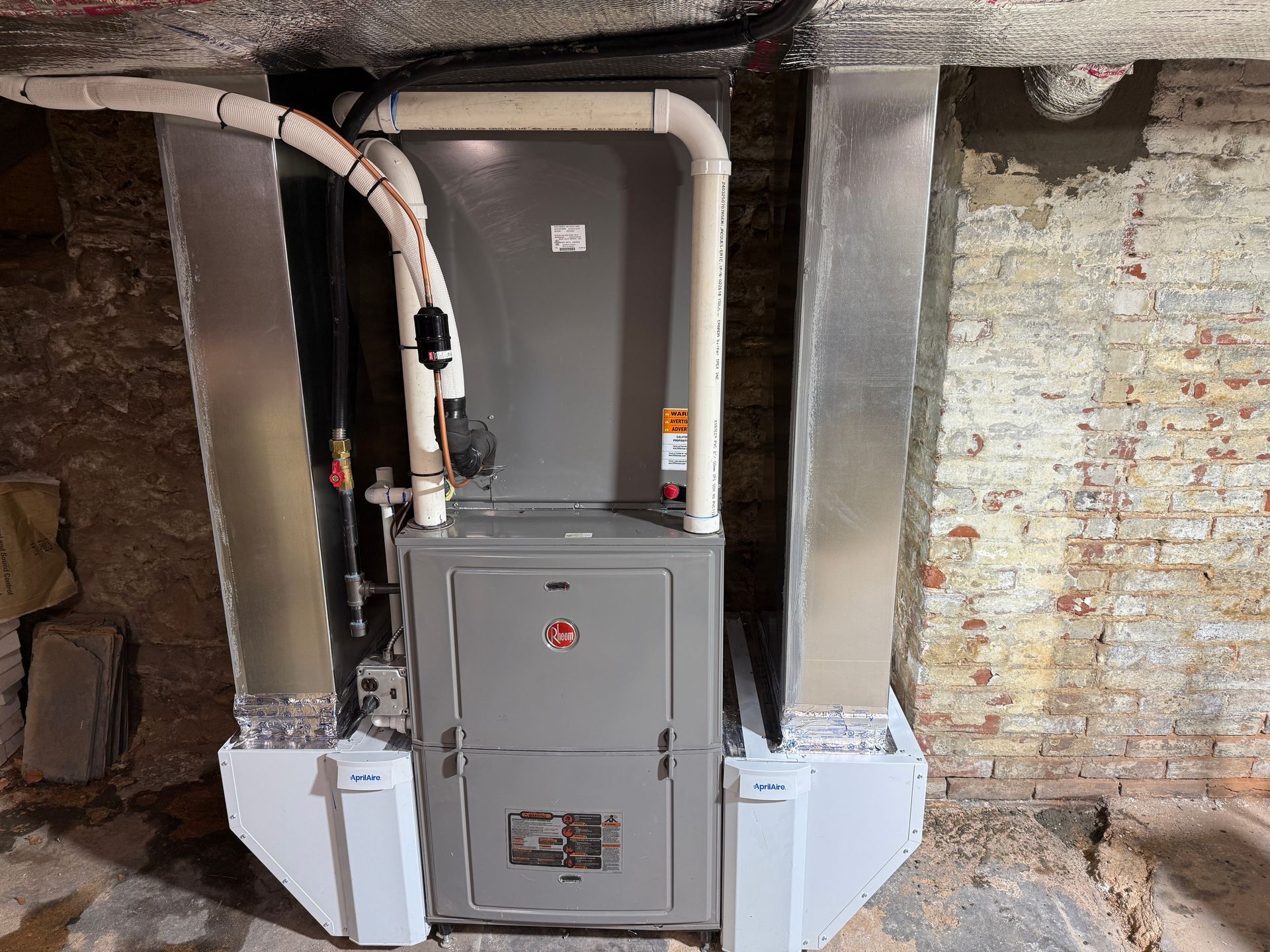 A gray HVAC system with ductwork installed in a brick-walled basement.