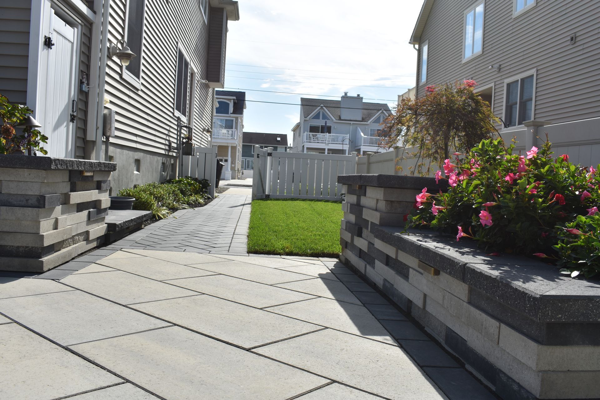 A brick walkway leading to a house with flowers in front of it