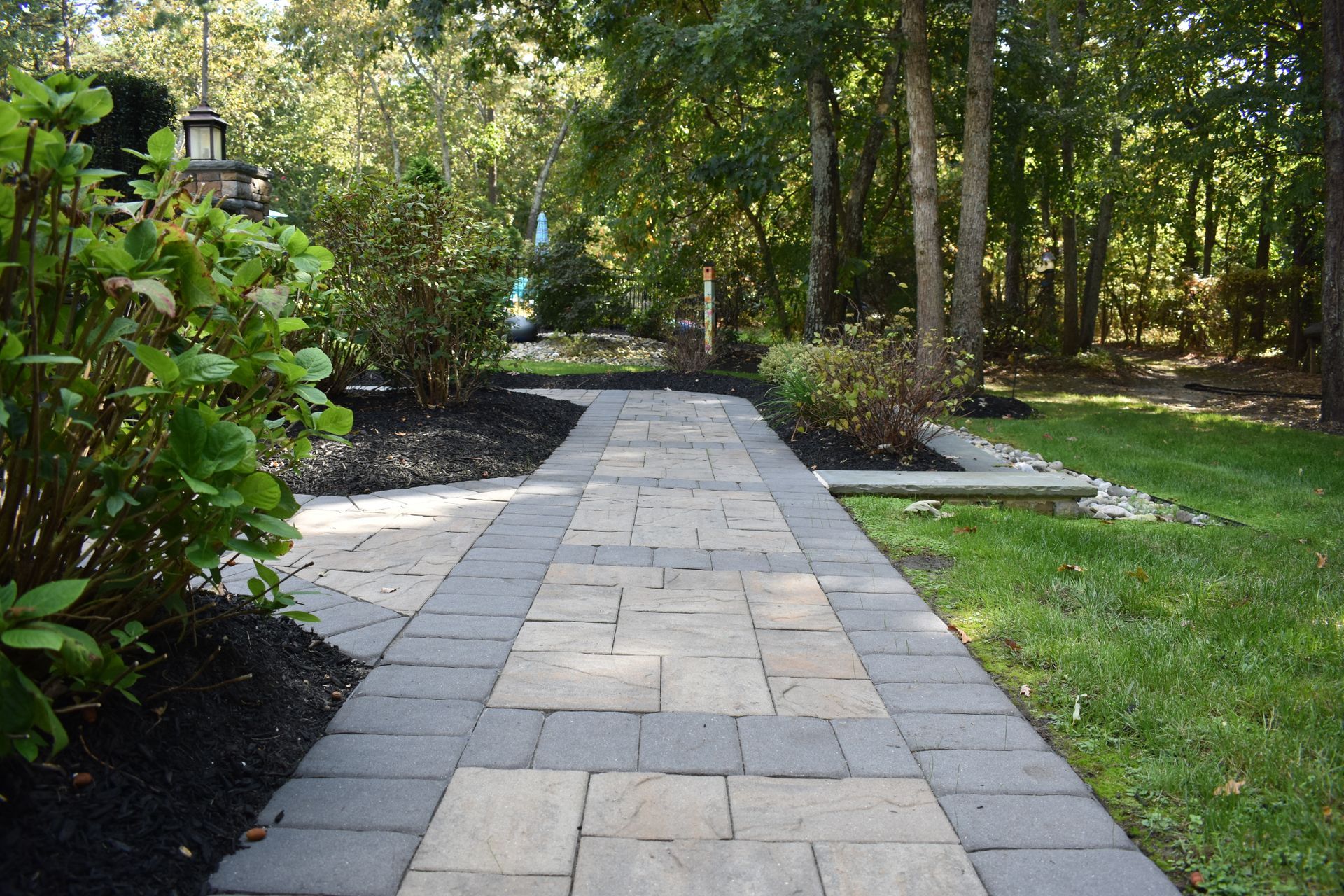 A brick walkway leading to a lush green forest.