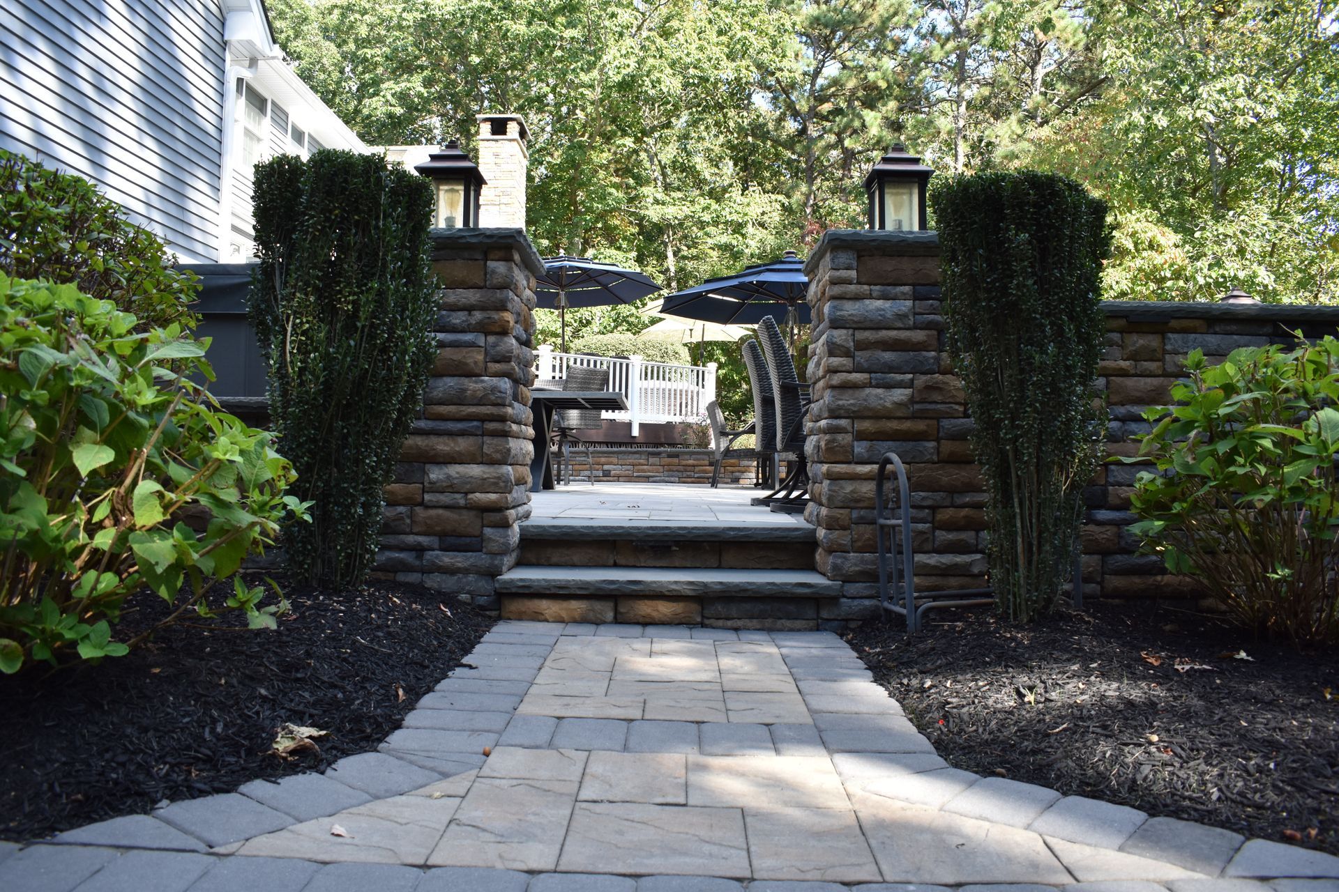 A stone walkway leading to a patio with umbrellas and chairs.
