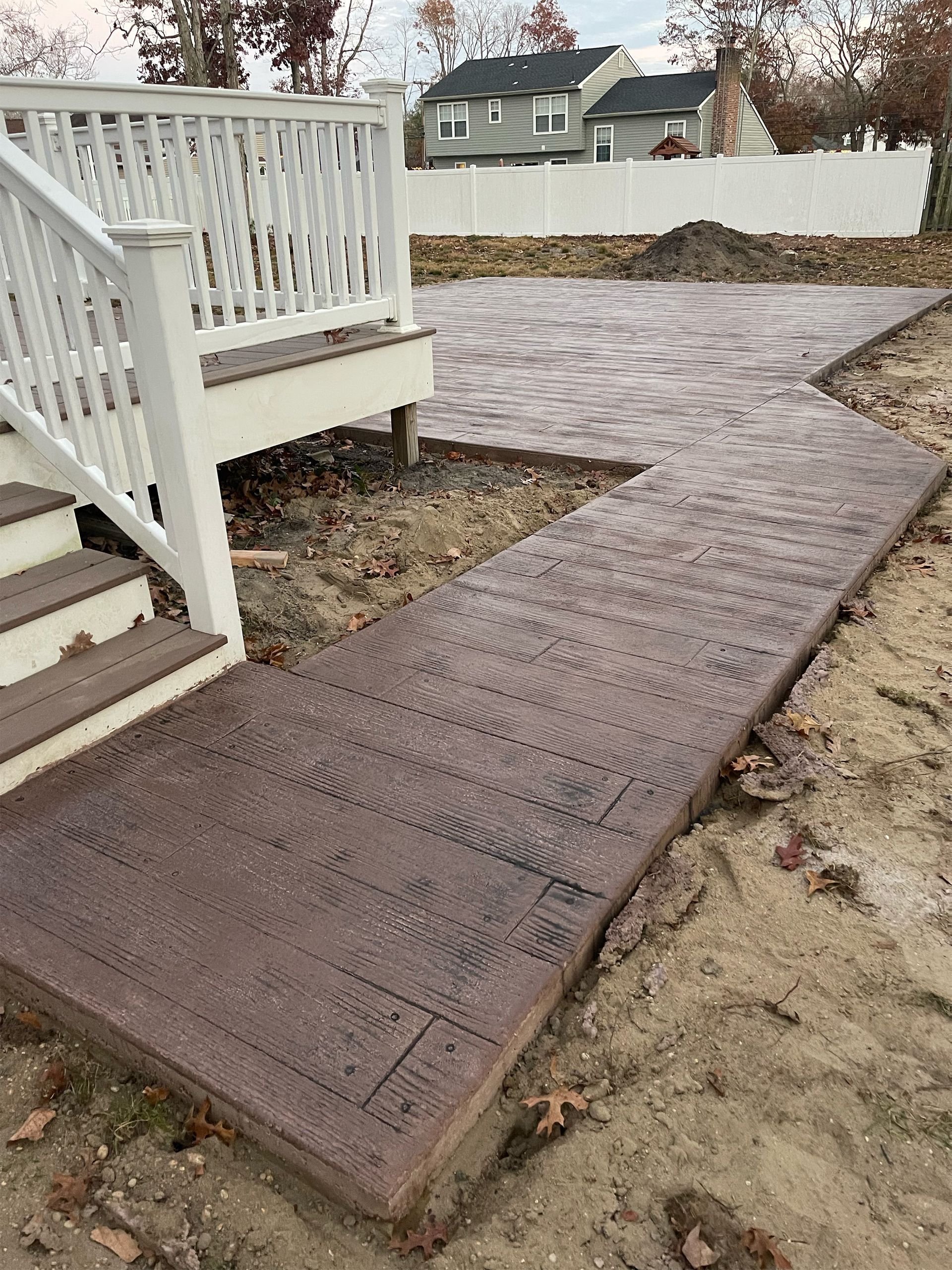 A concrete walkway leading to a deck with stairs and a white railing.