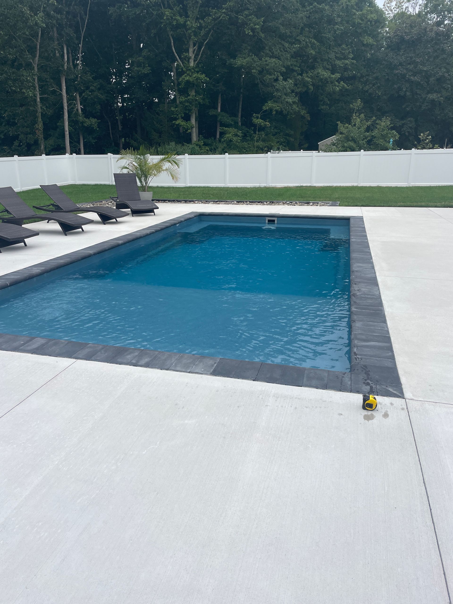 A large swimming pool is surrounded by chairs and a white fence.