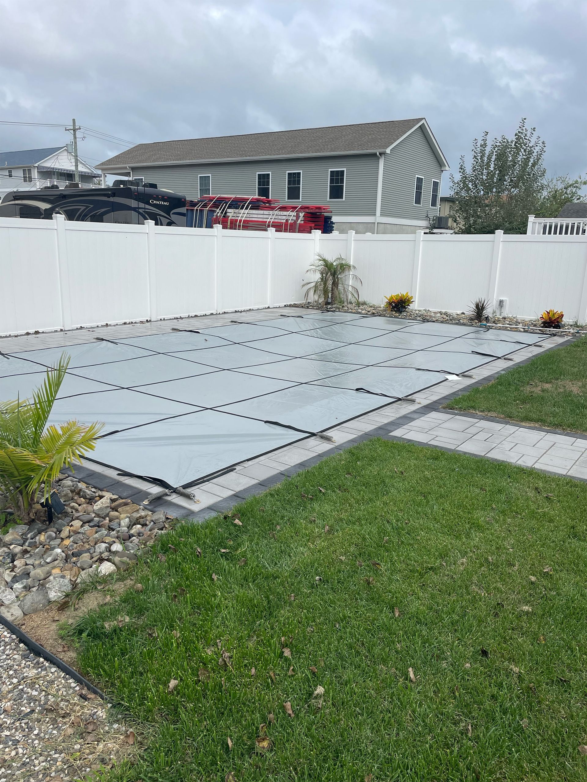 A white fence surrounds a swimming pool in a backyard.