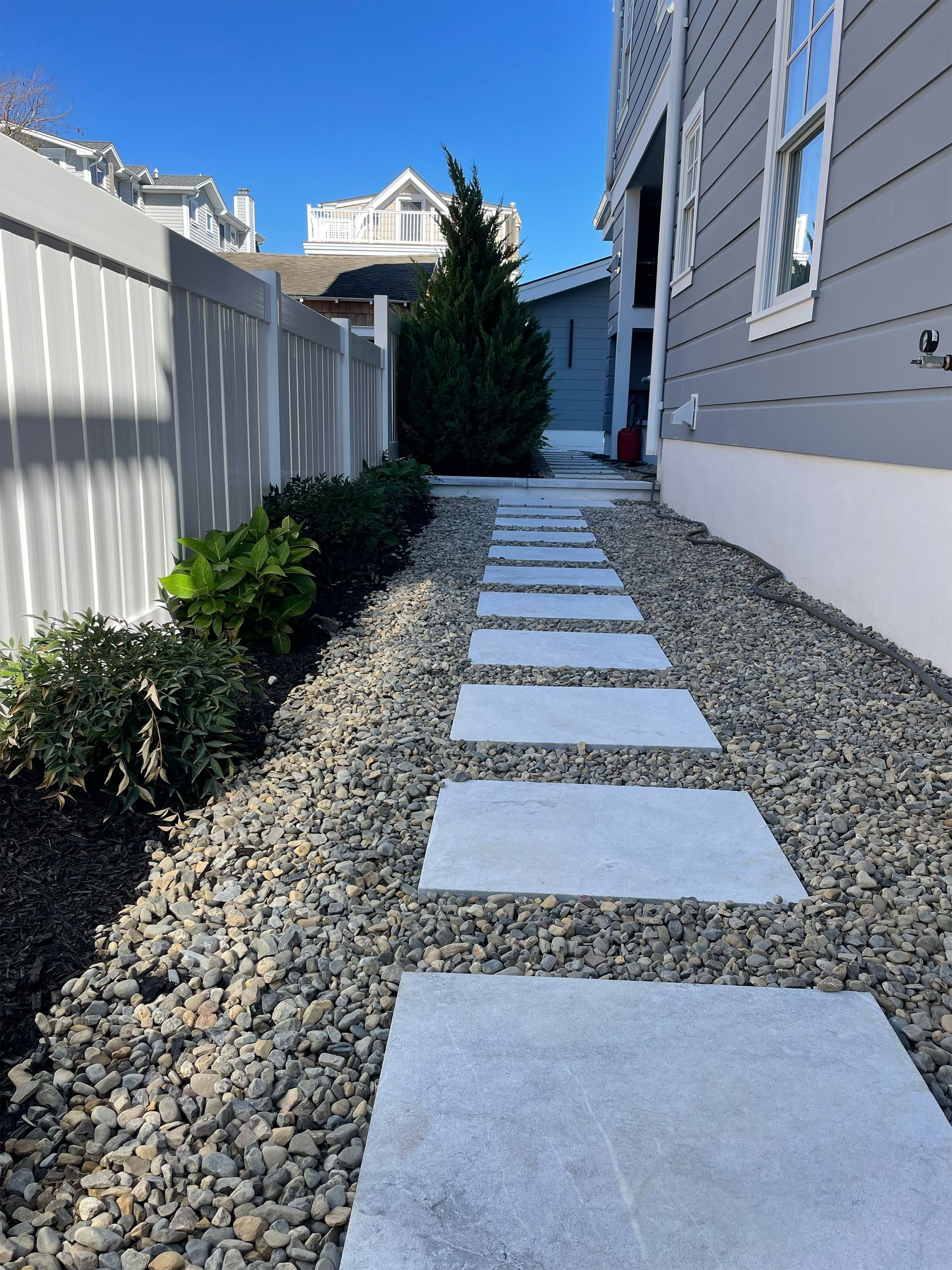 A stone walkway leading to a house with a white fence