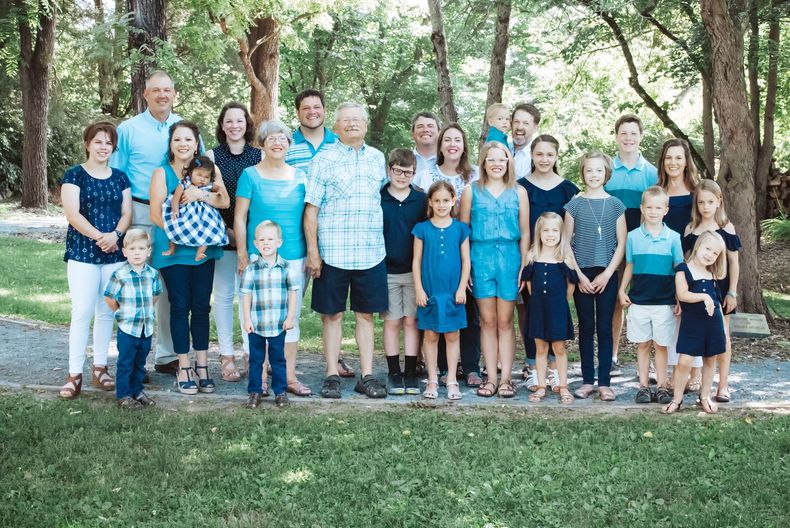 Large family group in a park, mostly wearing blue, smiling at the camera.