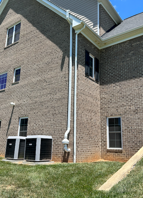 A large brick house with a white gutter on the side of it.