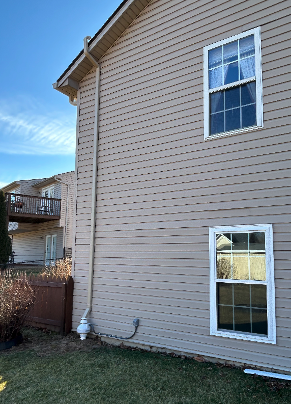 The side of a house with two windows and a drain pipe.