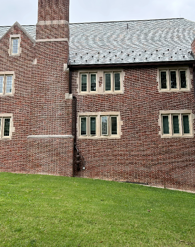 A large brick building with a gray roof is sitting on top of a lush green field.