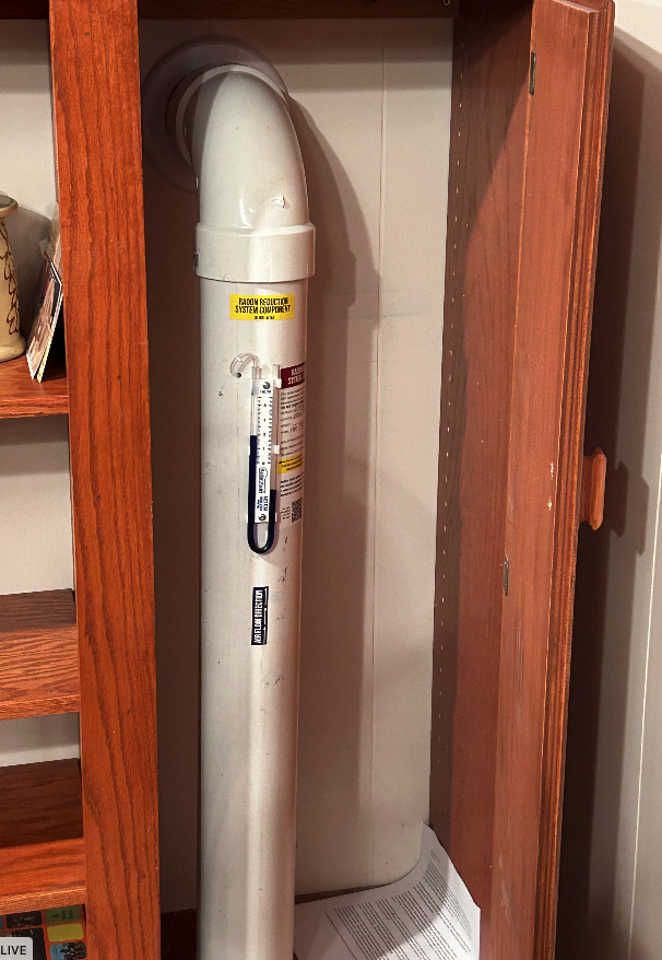 A white pipe with a yellow sticker on it is in a wooden cabinet.