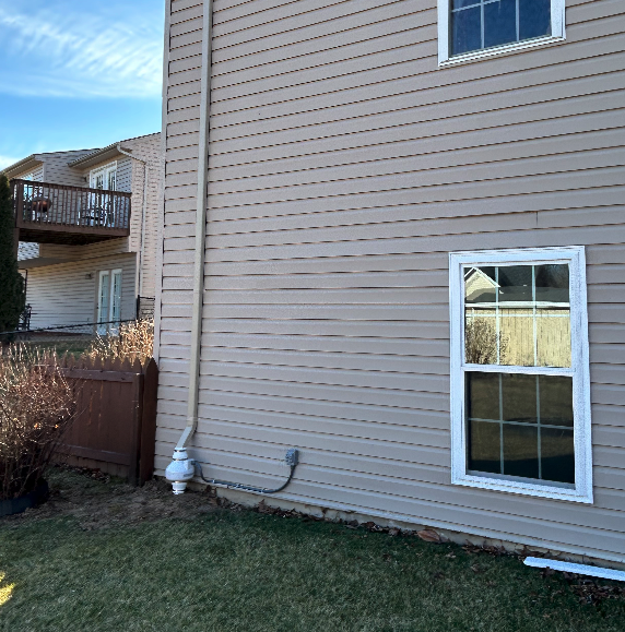 The side of a house with a window and a drain pipe.