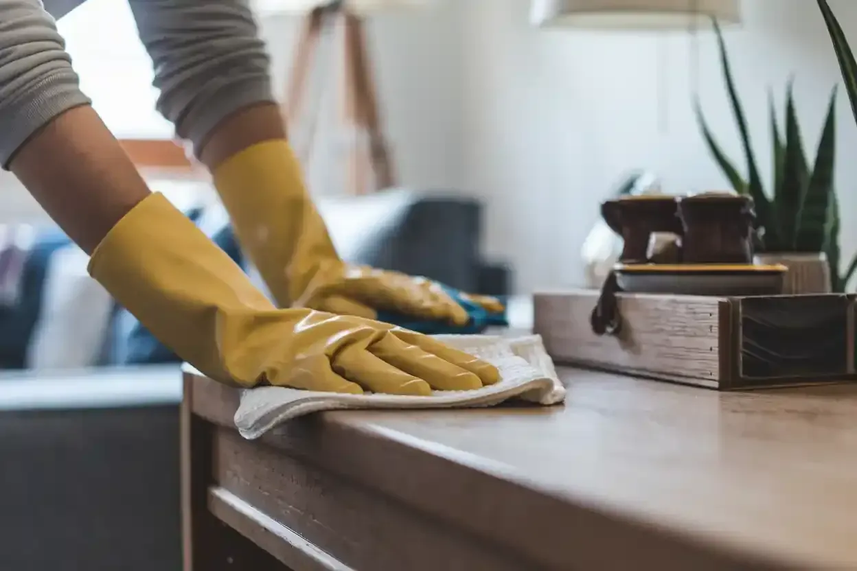A person wearing yellow rubber gloves is cleaning a table with a cloth.