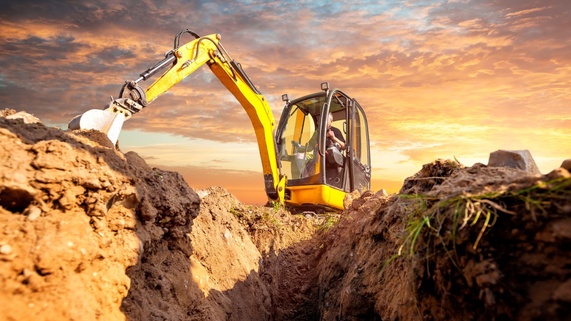 a yellow excavator is digging a trench in the dirt .