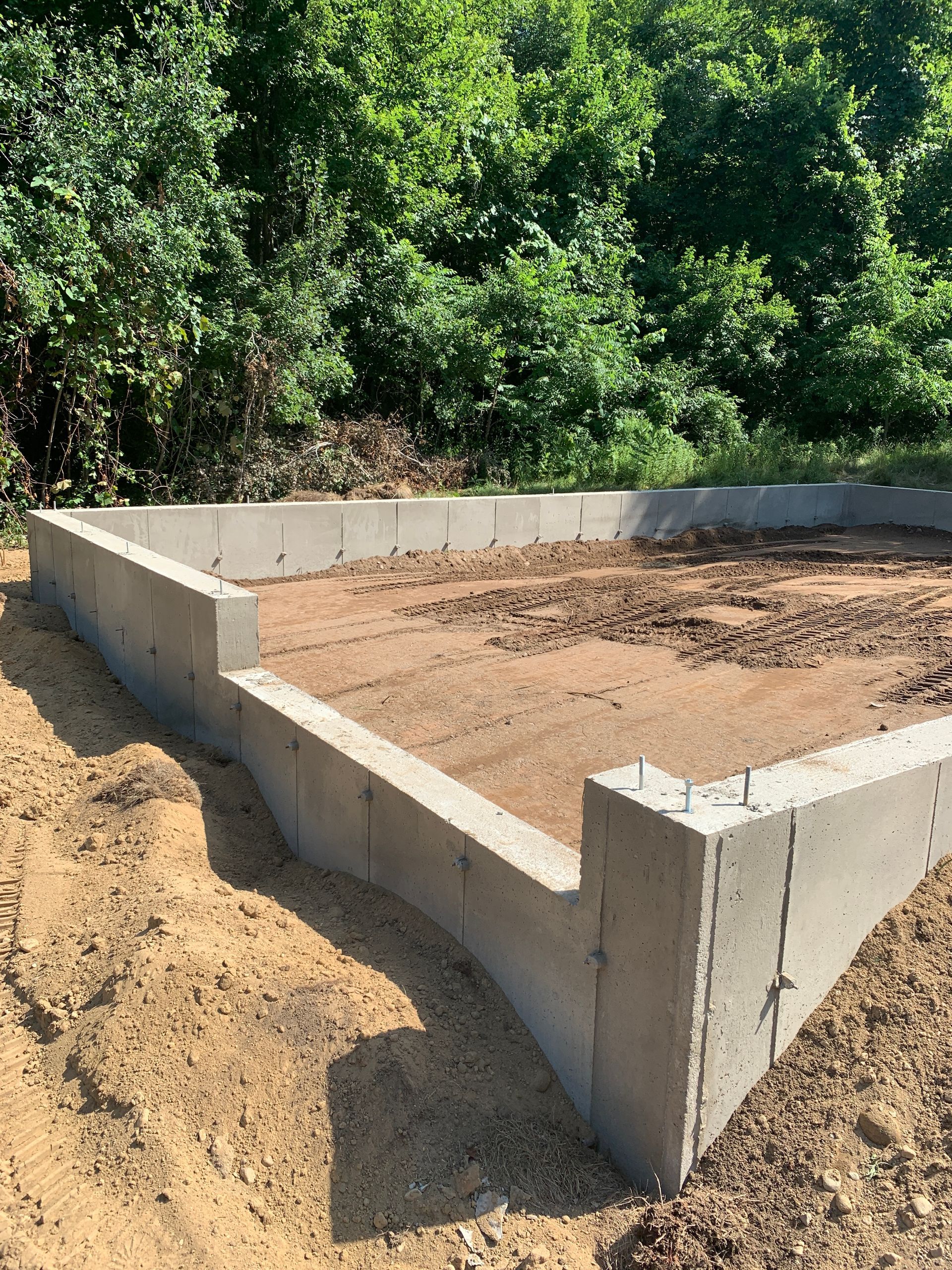 A concrete foundation is being built in a dirt field with trees in the background.
