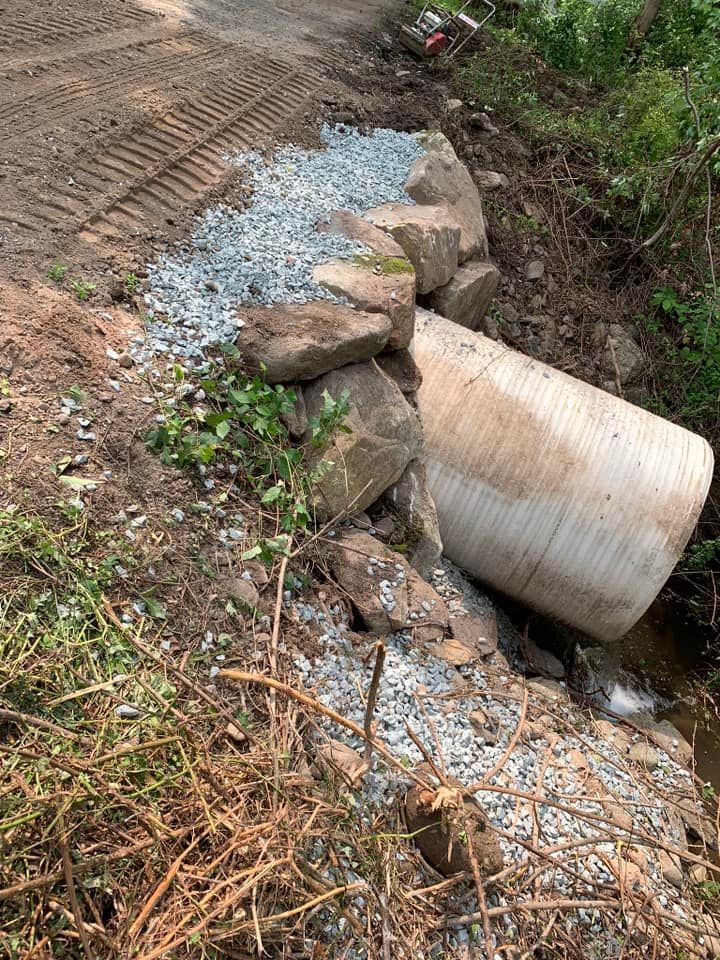 A large pipe is sitting on the side of a dirt road next to a stream.