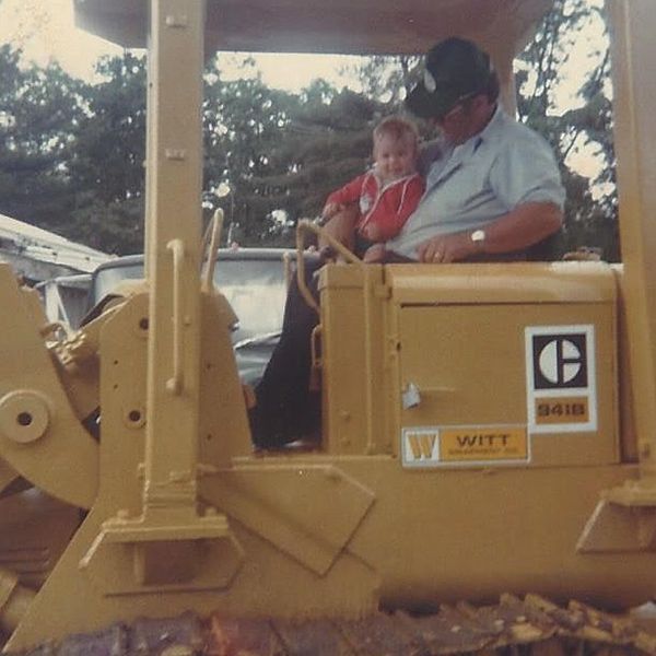 A man is driving a bulldozer with a child in the back seat