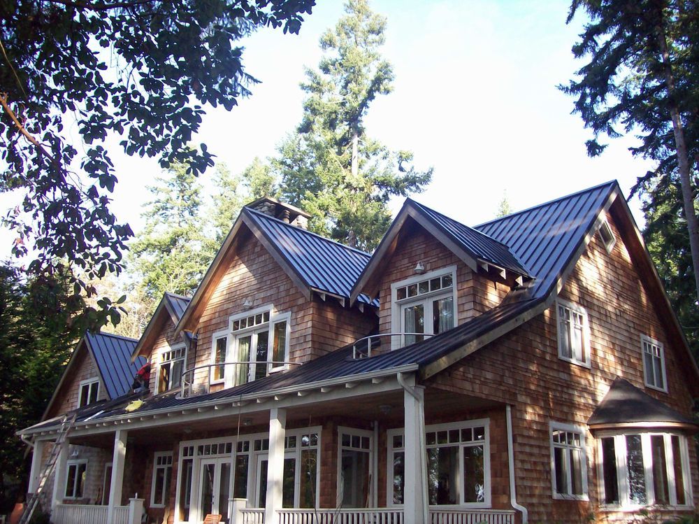 Wooden house with black metal roof and white trim, surrounded by trees.