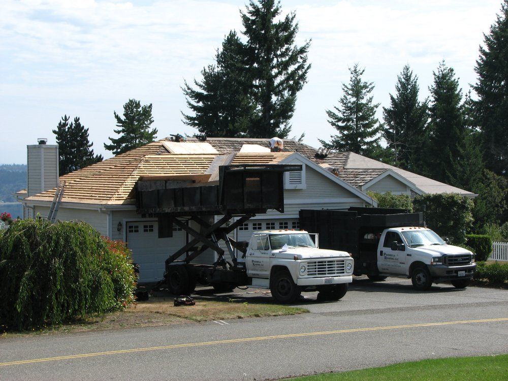 Roofers working on a house, using a lift and trucks on a sunny day.