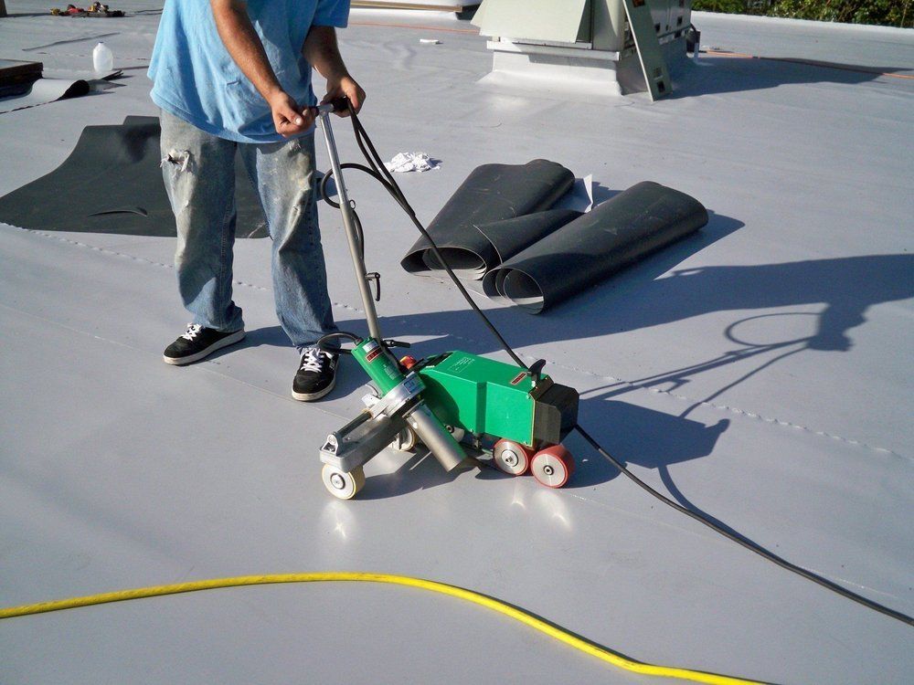 Person welding a gray, flat roof with a green machine.