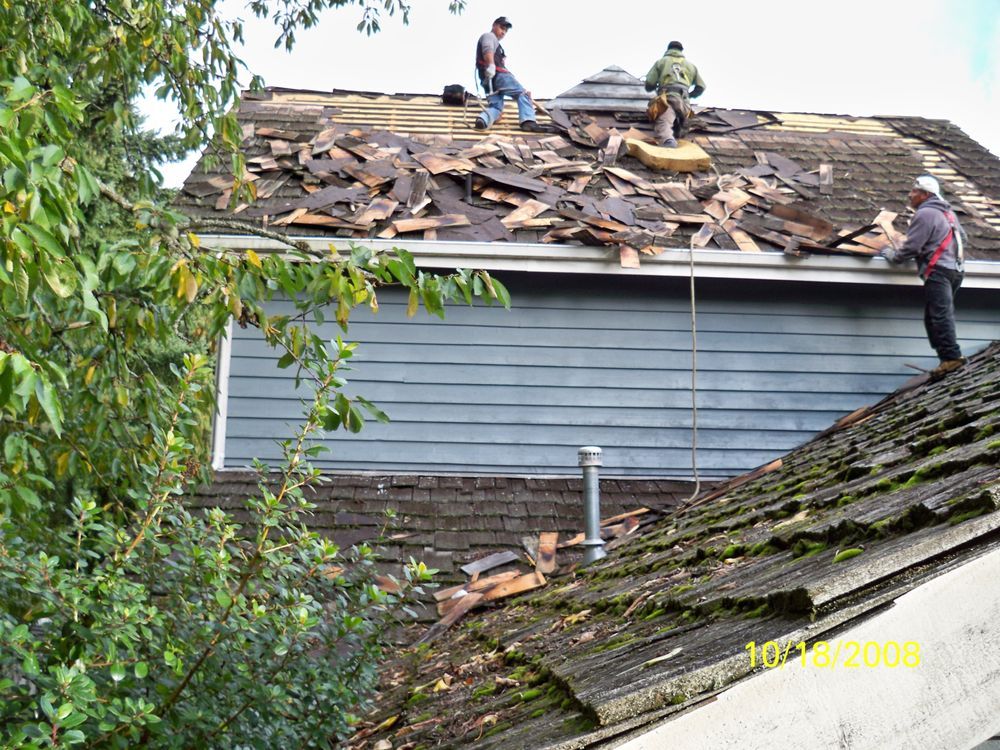 Men replacing roof shingles on a residential home with blue siding.