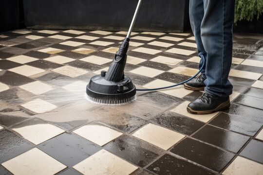 A man is cleaning a tiled floor with a high pressure washer.