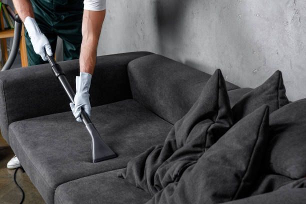 A man is cleaning a couch with a vacuum cleaner.