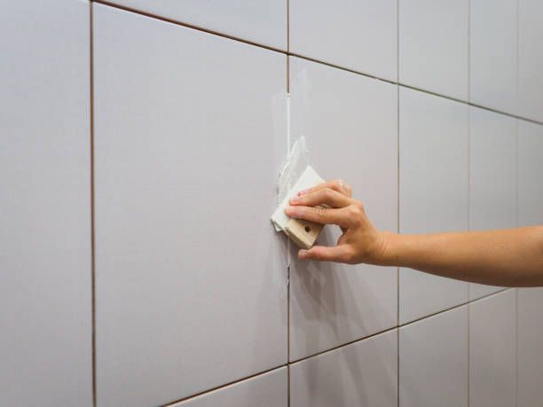 A person is cleaning a tile wall with a sponge.