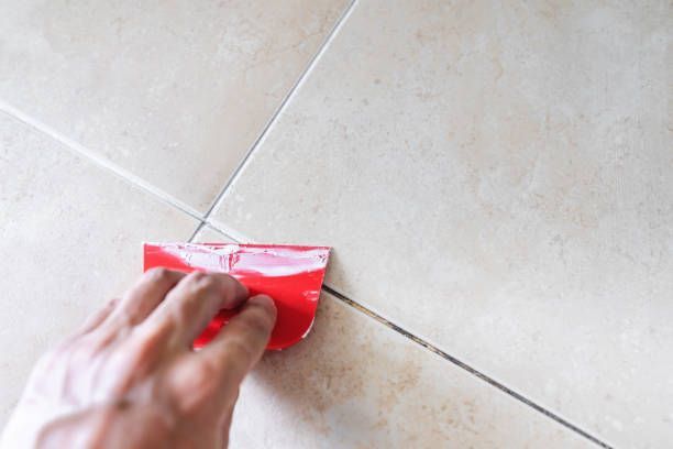 A person is cleaning a tile floor with a red spatula.