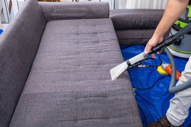 A man is cleaning a couch with a vacuum cleaner.