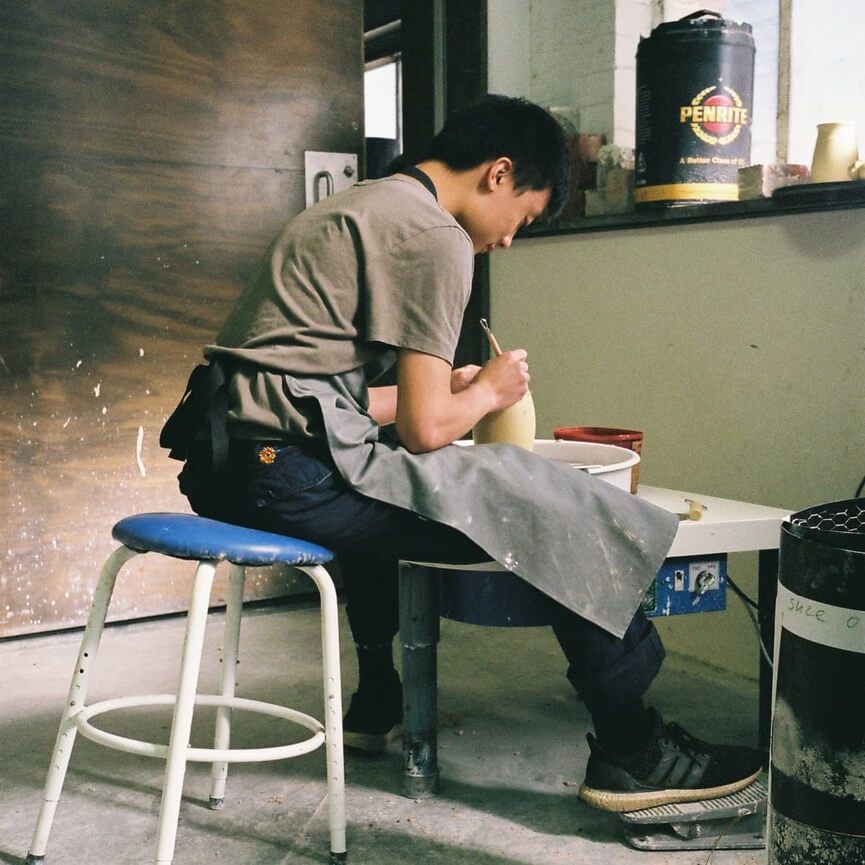 Angelo Ooi sits on a stool in his workshop and adds detailing to a ceramic vessel