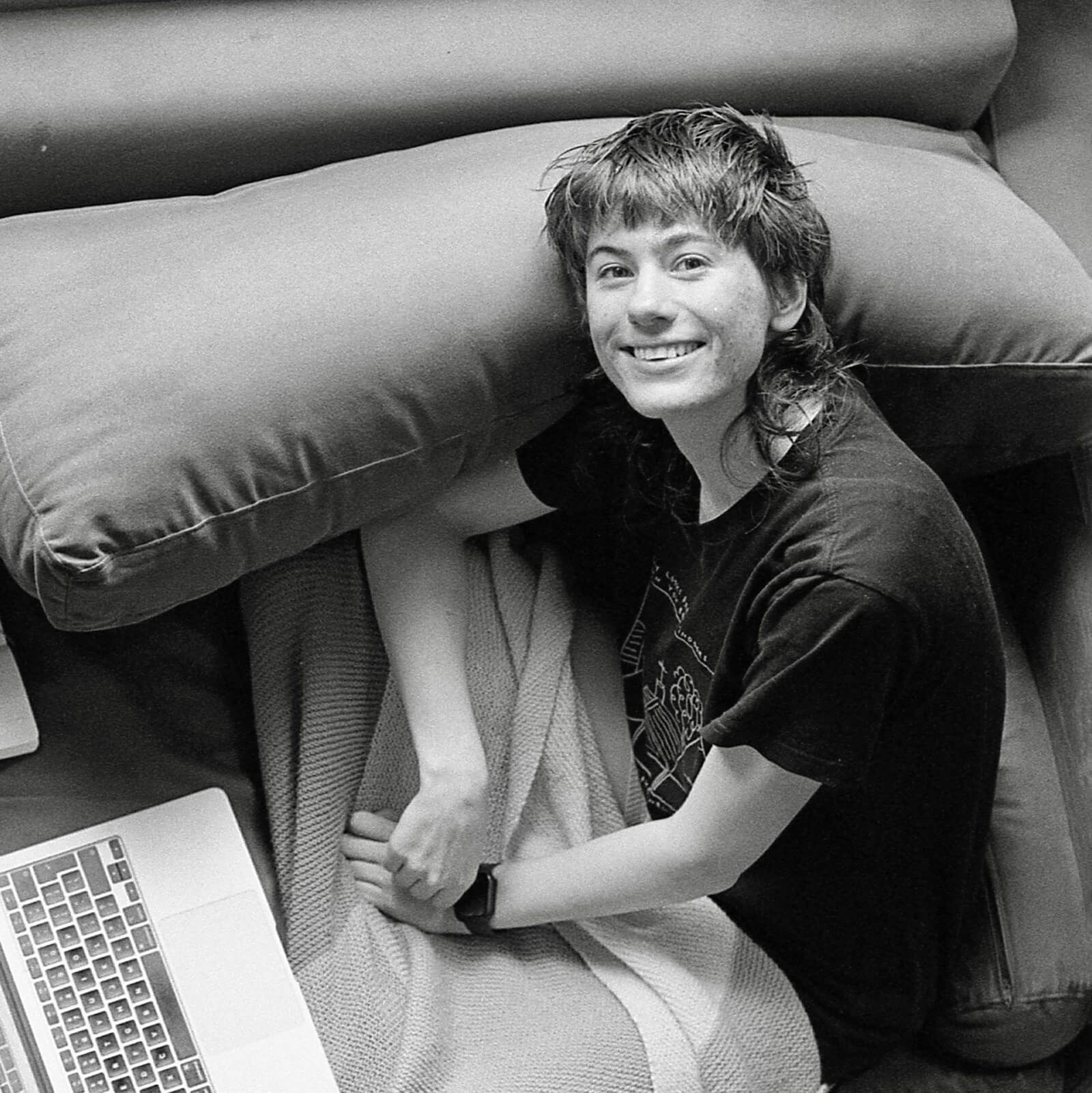 Em Constance, a designer, sits on a couch with their laptop open in front of them