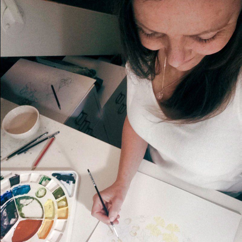 Helen Castles sits at a desk, painting an intricate watercolour piece using a fine paintbrush