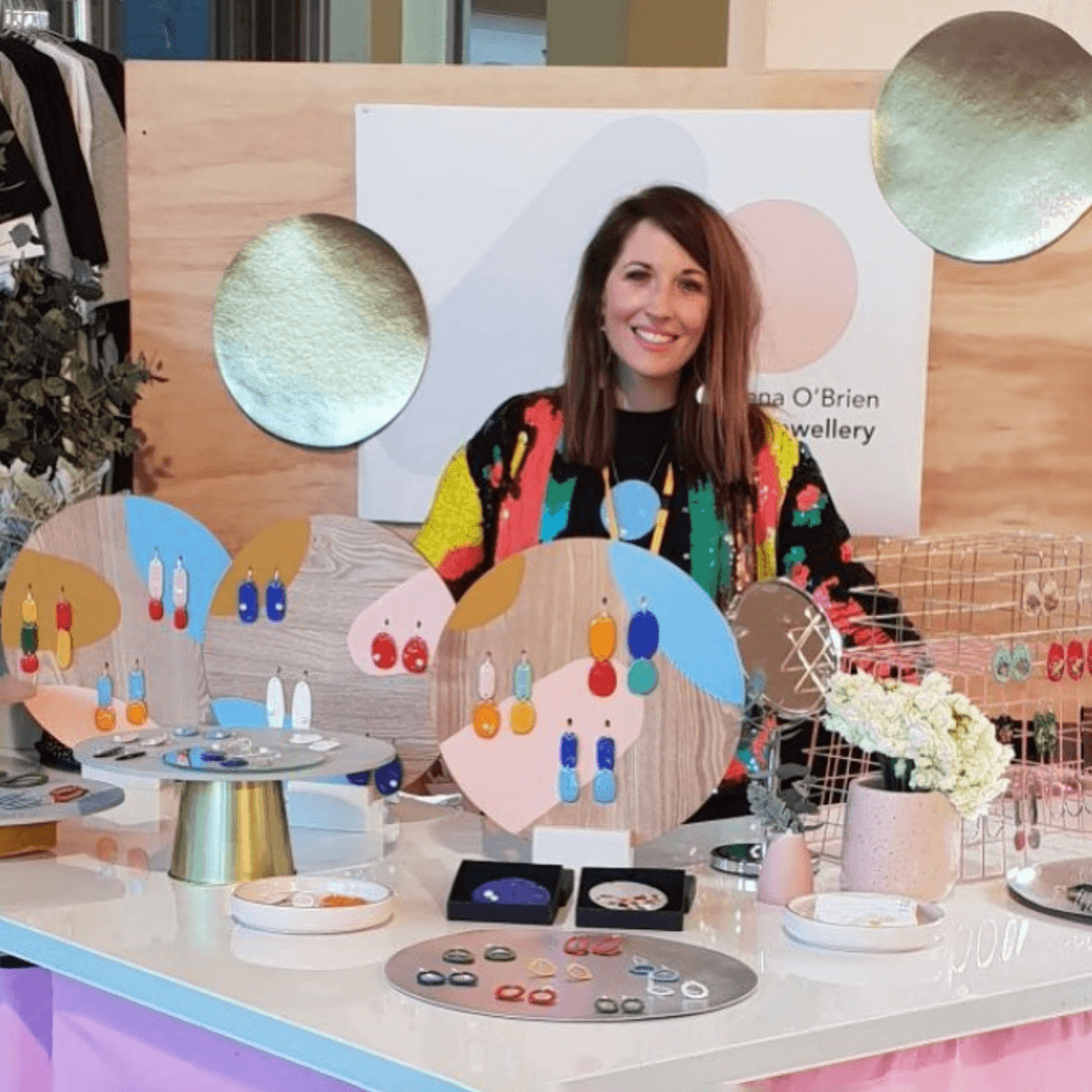 Jenna O’Brien sits at a market table selling colourful enamel jewellery