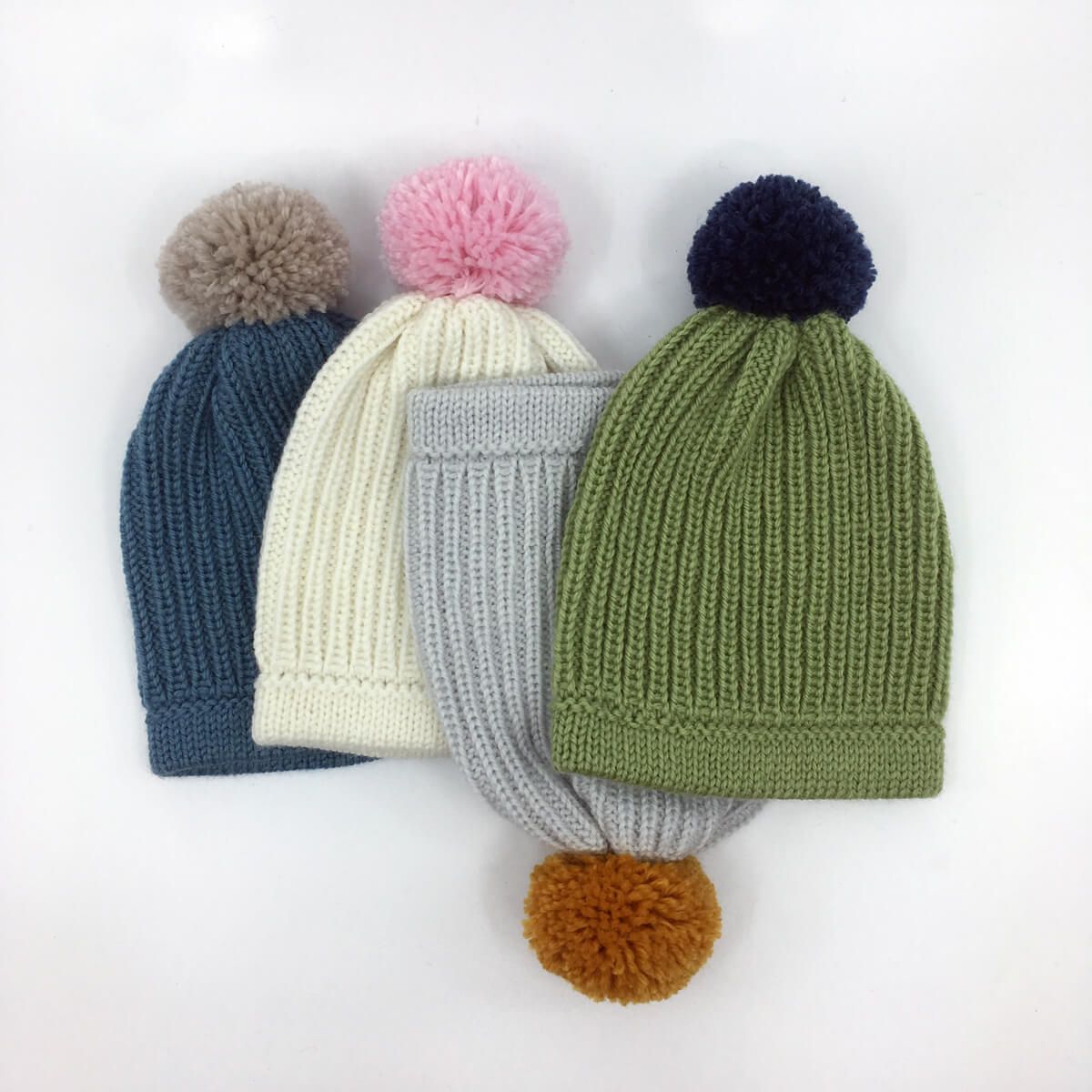 four woollen baby beanies in various colours, with woollen pom-poms on top of each