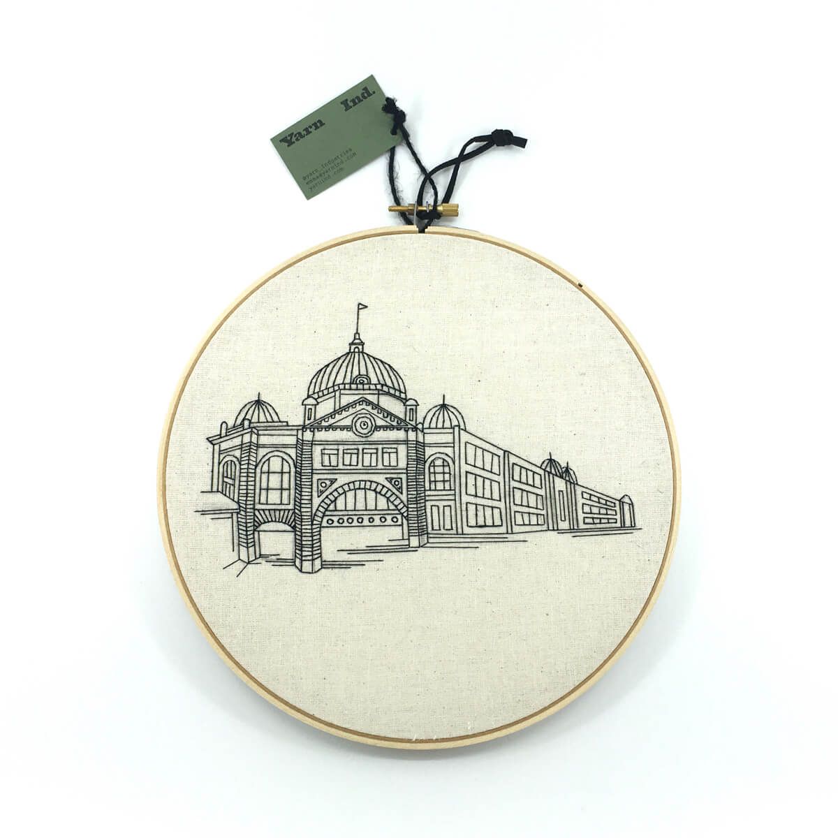 an embroidered image of Flinders Street station, black thread on cream fabric in an embroidery hoop