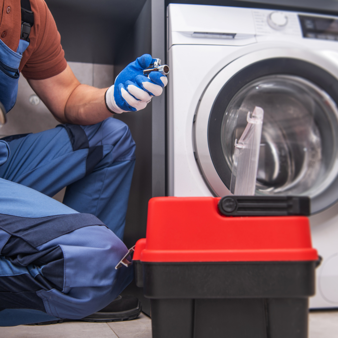 Un hombre está trabajando en una lavadora junto a una caja de herramientas.