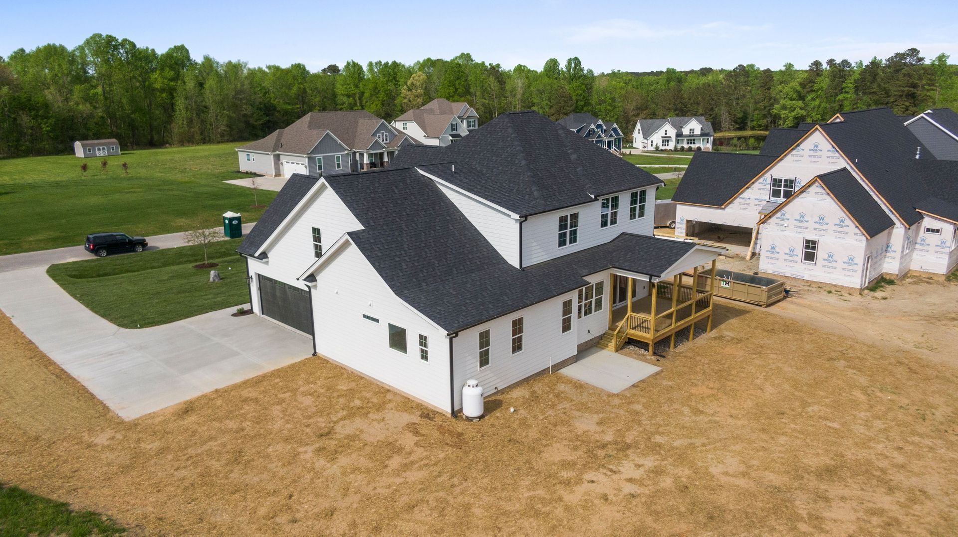 New white two-story house with dark roof in a suburban neighborhood, front porch under construction.