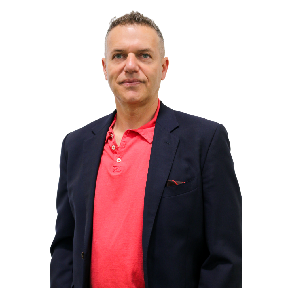 A man in a suit and a red shirt is standing in front of a white background.