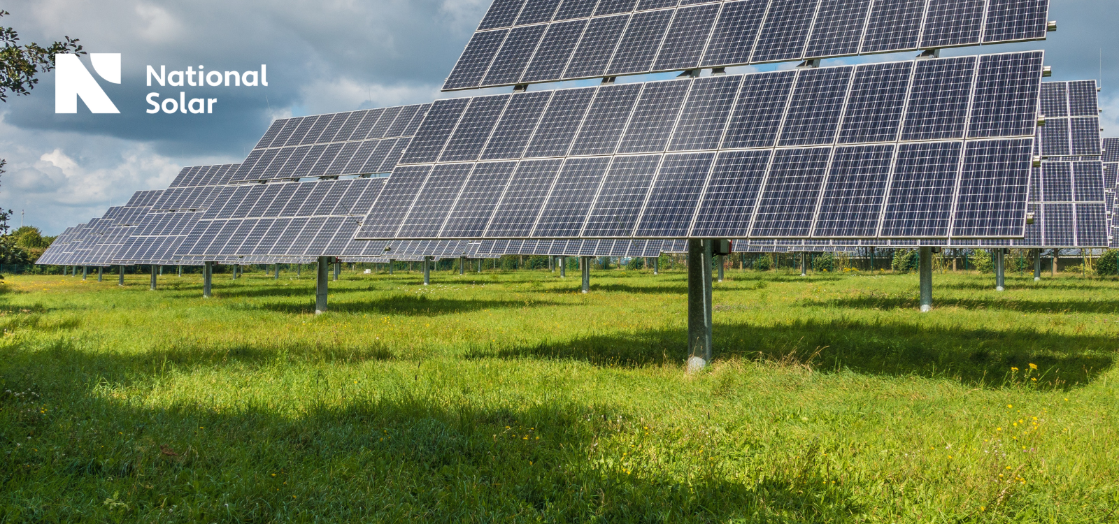 A row of solar panels in a grassy field with a national solar logo in the background