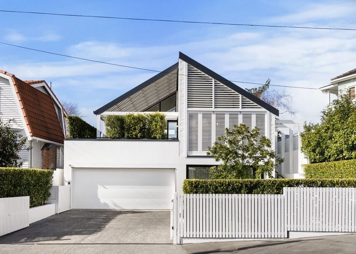 Modern white house with angled roof, black accents, garage, and manicured hedge.