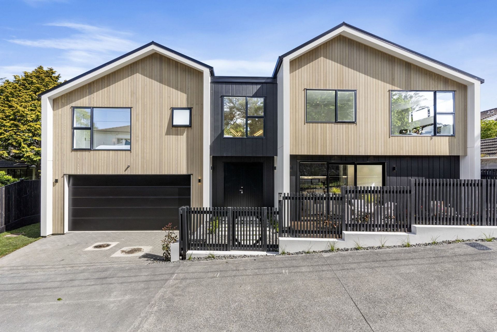 Modern two-story home with wood siding, black accents, and a garage. Set on a slight slope with a black fence.