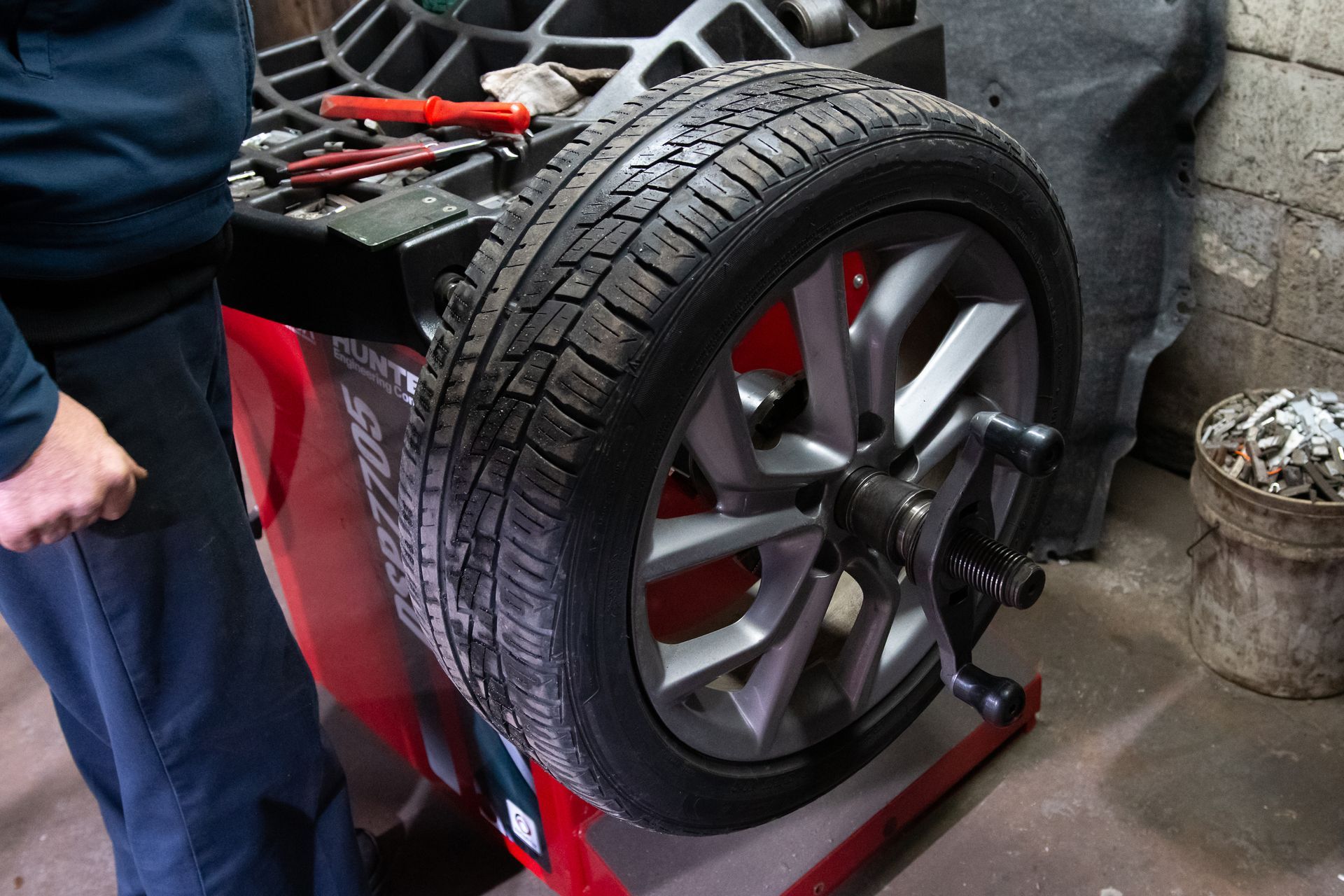Tire on a balancing machine in a garage; a person stands nearby.