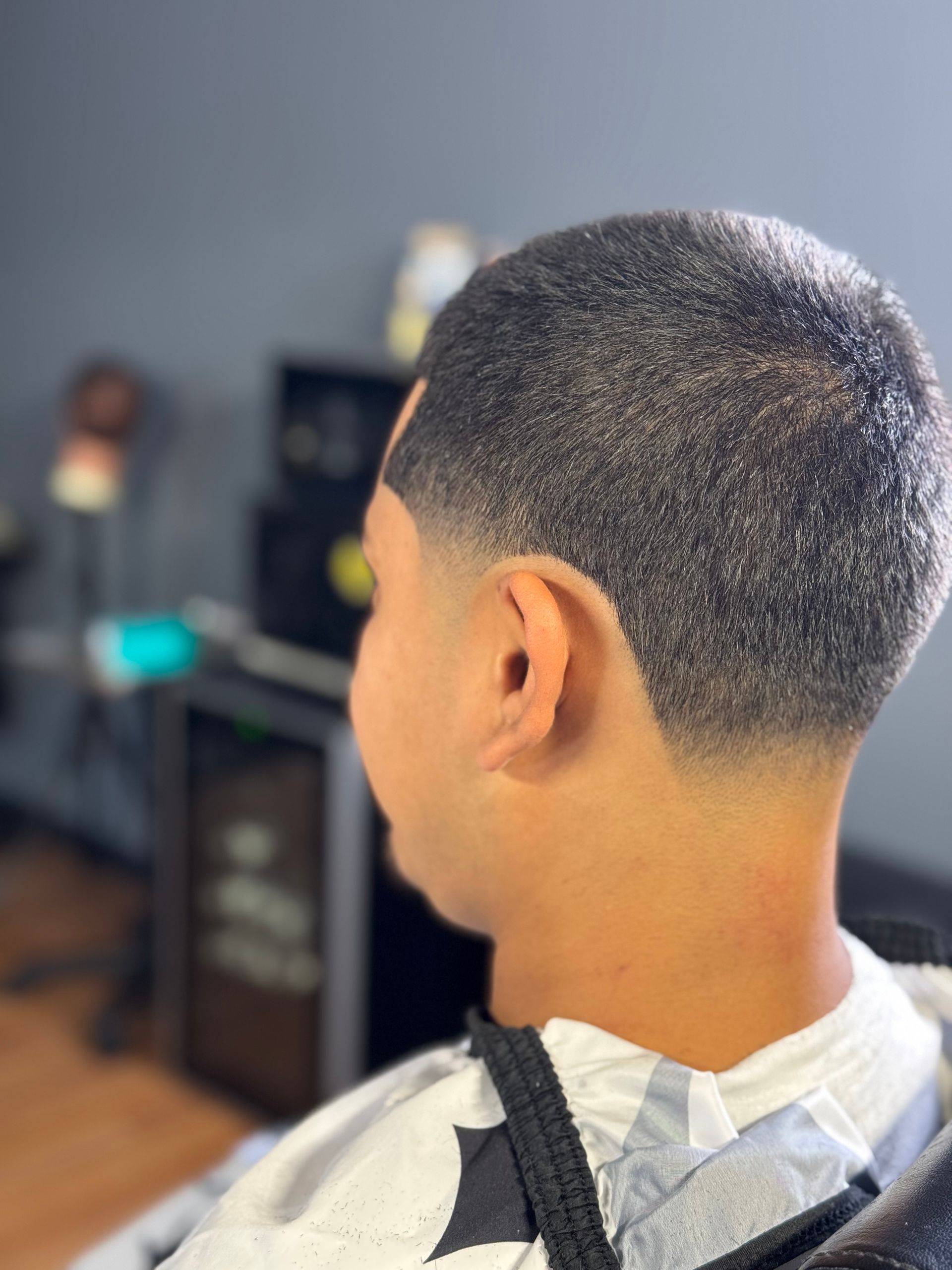 A person with a dark, textured haircut, featuring a skin fade. They're seated in a barbershop.