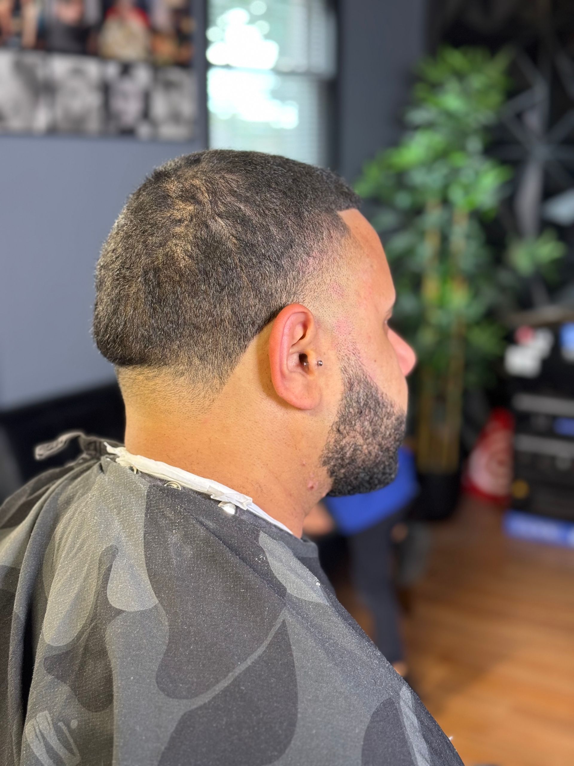 Man with fade haircut, beard, and barber's cape at a barbershop.